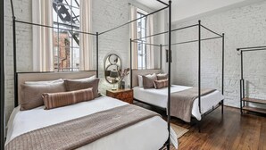 Een kamer met twee bedden, witte muren, een bakstenen muur en een raam met gordijnen.