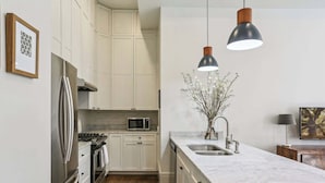 Een moderne keuken met witte kasten, roestvrijstalen apparatuur, een marmeren aanrecht en hanglampen.