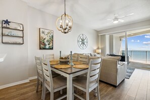 Ein Essbereich mit einem Holztisch, weißen Stühlen und einer Kristallleuchter. An der Wand hängt ein Gemälde, und eine Kompassdeko ist vorhanden.