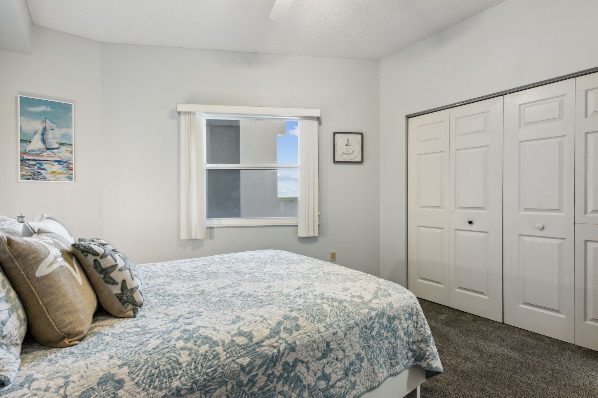 A bedroom with a bed, a window, a closet, and a painting on the wall.