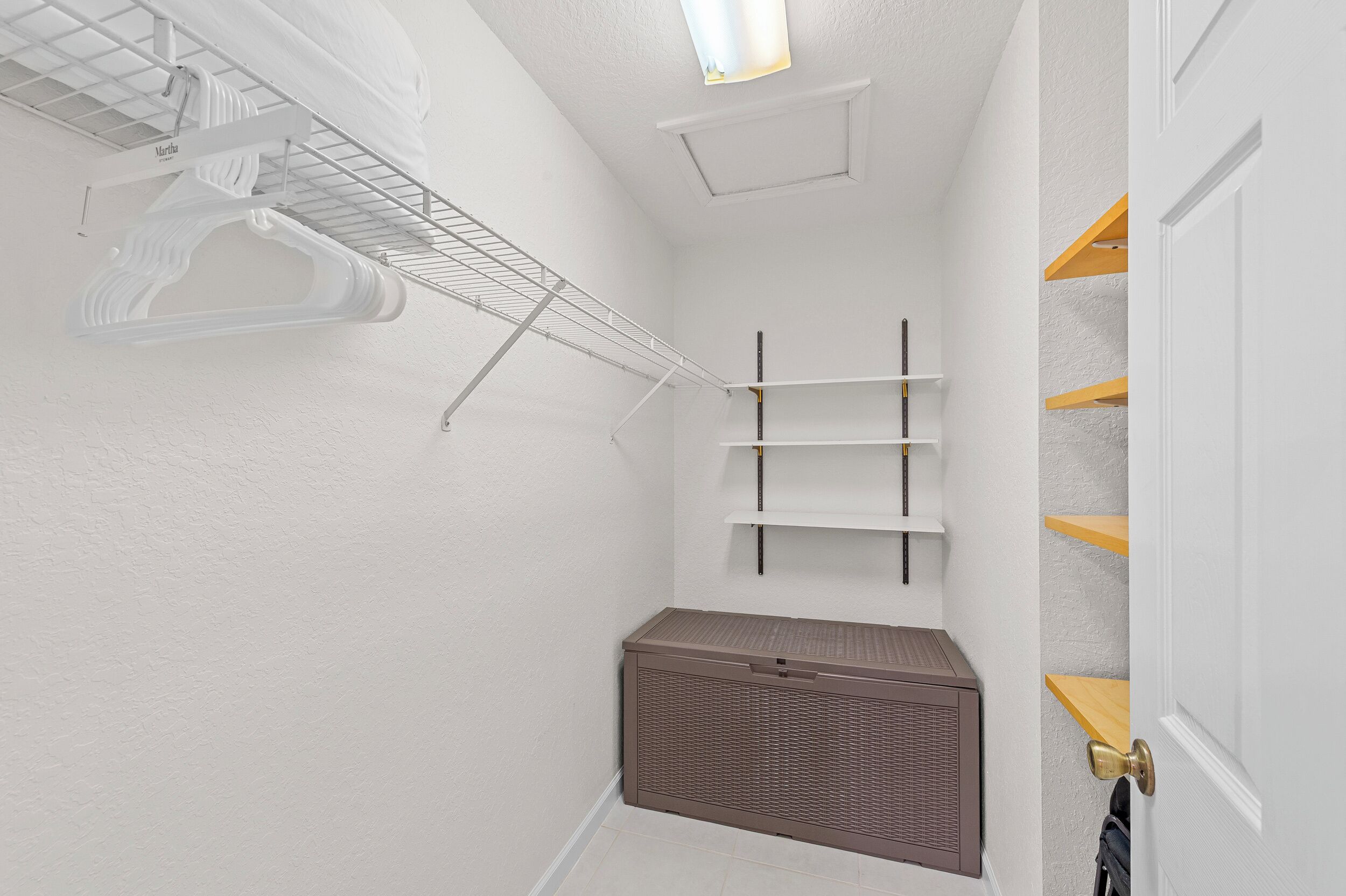 A laundry room with a metal rack, shelves, and a chest of drawers.