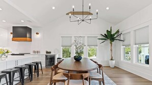 A spacious kitchen with a central island, wooden chairs, and a chandelier. - Modern 6BR Beach Retreat w/ Private Pool (Oak Island)