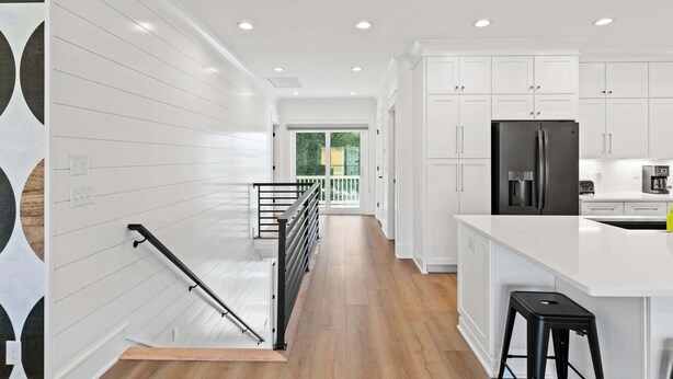 A modern kitchen with white cabinetry, a black refrigerator, and a wooden floor. - Modern 6BR Beach Retreat w/ Private Pool (Oak Island)