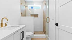 Ein modernes Badezimmer mit einer Duschkabine, einer Toilette und einem Waschbecken mit goldfarbenen Armaturen.