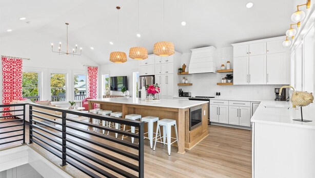 Een moderne keuken met witte kasten, een centraal eiland met krukken, hanglampen en uitzicht op de omgeving.