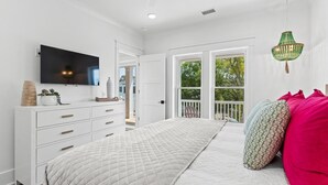 Een slaapkamer met een bed, een dressoir, een televisie en een raam met uitzicht op bomen.