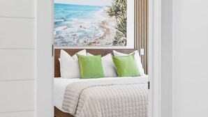 Een slaapkamer met een bed, wit beddengoed en een schilderij van een strand.