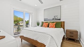 Une chambre avec un grand lit, une table de chevet en bois, une commode blanche et une vue sur l’extérieur.
