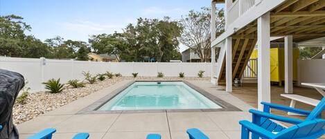 A backyard with a swimming pool, blue lounge chairs, and a covered patio area.