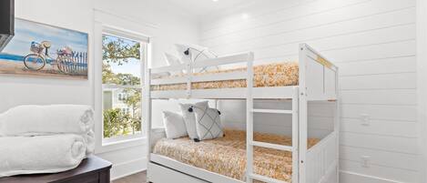 A bunk bed with floral bedding, a window with a view of a house and trees, and a painting of a bicycle on the wall.