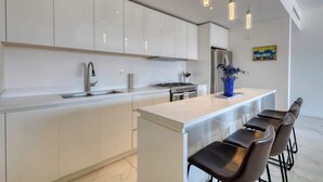 Une cuisine moderne avec des meubles blancs, un évier en acier inoxydable et un îlot central doté de tabourets de bar.