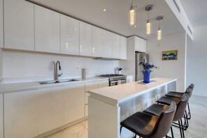 A modern kitchen with white cabinets, a stainless steel sink, and a central island with bar stools. - Modern condo near Medano beach (Cabo San Lucas)