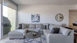 Un salon moderne avec un canapé d’angle gris, une petite table basse ronde et une grande fenêtre donnant sur l’extérieur.