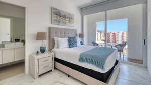 Une chambre moderne avec un grand lit, une table de chevet, un miroir et une vue sur la ville grâce à une porte-fenêtre coulissante.