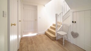 A hallway with a wooden floor, a white door, and a staircase with beige carpeted steps. - Charming Barn Conversion, Idyllic Somerset Village (Somerset)