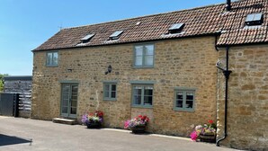 A stone building with a tiled roof, multiple windows, and flower planters along the front. - Charming Barn Conversion, Idyllic Somerset Village (Somerset)