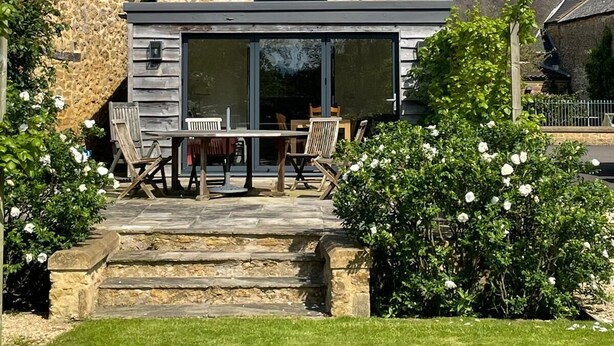 A stone house with a large window and a balcony, surrounded by a well-maintained garden. - Charming Barn Conversion, Idyllic Somerset Village (Somerset)