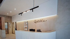Um balcão de recepção moderno com uma placa com o nome 'Quadrato', painel de parede de madeira e luminária suspensa no teto.