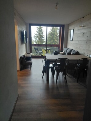 A modern interior with a dining area, a sofa, and a view through large windows. - Le Corbier: a new, cozy apartment right in the heart of the resort! (Villarembert)