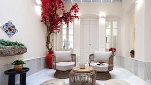Ein gemütlicher Sitzbereich mit Korbstühlen, Poufs und einem kleinen Tisch mit Kerzen, sowie ein Blumentopf.