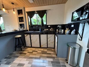 Una cocina moderna con una isla de mármol, taburetes de bar, una cafetera y un televisor montado en la pared.