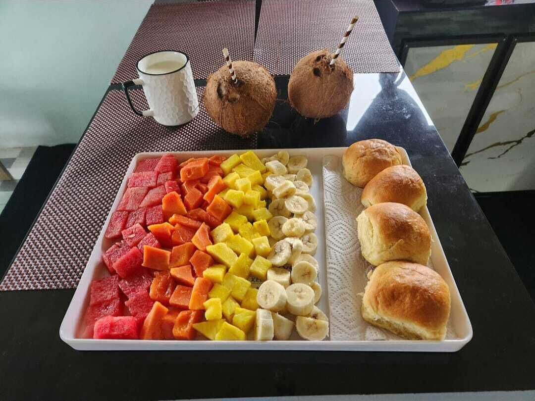 Una bandeja con fruta y pasteles sobre una mesa, junto a una taza de café y dos cocos.