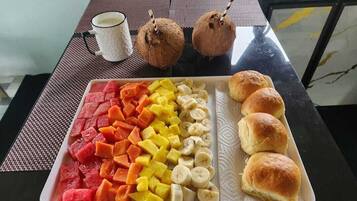 Una bandeja con fruta y pasteles sobre una mesa, junto a una taza de café y dos cocos.