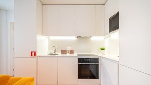 Una cocina compacta con muebles blancos, un horno empotrado y una cafetera sobre la encimera.