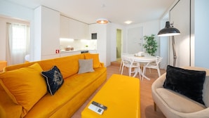 Una sala de estar moderna con un sofá amarillo, una mesa de comedor blanca con sillas y una lámpara de pie.