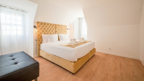 A bedroom with a bed, a bedside table, a lamp, and a window with curtains. - Guestready - The Corner 2E (Lisbon)