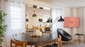 A modern dining area with a round table, chairs, a lamp, and a television displaying 'GUEST READY'. - Guestready - The Corner 2E (Lisbon)
