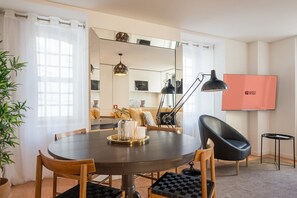 Ein moderner Essbereich mit einem runden Tisch, Stühlen, einer Lampe und einem Fernseher, der 'GUEST READY' anzeigt.