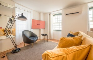 Ein modernes Wohnzimmer mit Sofa, Sessel, Stehlampe, Flachbildfernseher und einem kleinen Tisch.