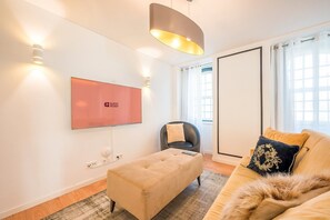A modern living room with a flat-screen TV, a sofa, a chair, and a pendant light. - Guestready - The Corner 2D (Lisbon)