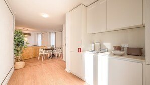 A modern kitchen with white cabinets, a dining area with a table and chairs, and a plant in the corner. - Guestready - The Corner 2D (Lisbon)