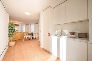 A modern kitchen with white cabinets, a dining area with a table and chairs, and a plant in the corner. - Guestready - The Corner 2D (Lisbon)