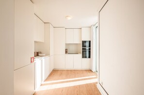 A narrow hallway leading to a kitchen with white cabinets, a wooden floor, and a built-in oven. - Guestready - The Corner 2D (Lisbon)