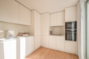 A compact kitchen with white cabinetry, a stainless steel oven, and a wooden floor. - Guestready - The Corner 2D (Lisbon)
