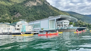 A waterfront building with a large glass facade, kayaks on the water, and a mountainous backdrop. - An ancient fresco above the gaze, the history around and the charm of Sarnico. (Sarnico)
