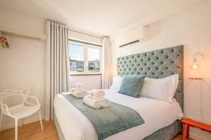 Una camera d'albergo con un letto grande, una finestra con tende, una sedia, un comodino e una lampada a parete.