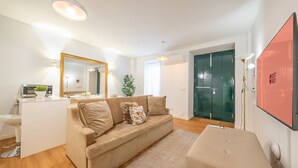 Un salon moderne avec un canapé beige, une petite table, un miroir et une porte verte.