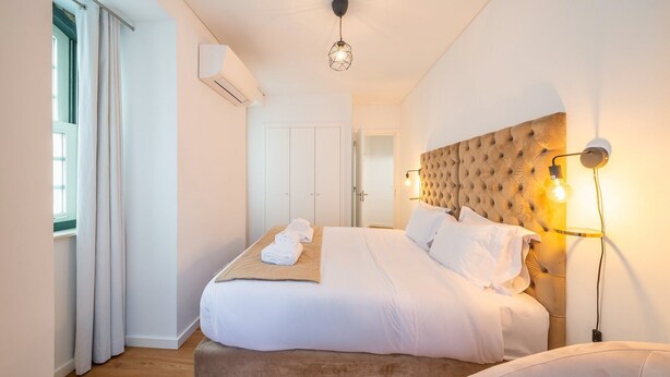Une chambre d’hôtel avec un grand lit, une tête de lit dotée d’un luminaire, un appareil de climatisation et une vue sur le couloir.