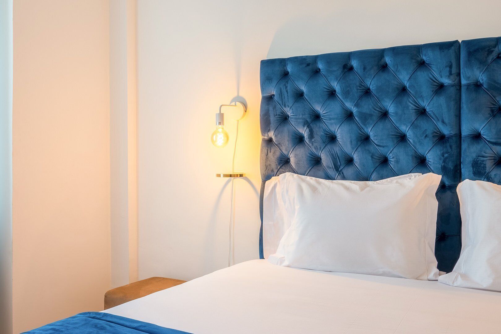 A bed with a tufted headboard, white pillows, and a bedside table with a lamp.