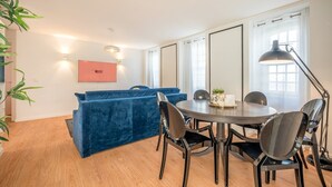Ein modernes Zimmer mit einem runden Esstisch, einem blauen Sofa und einem Flachbildfernseher.