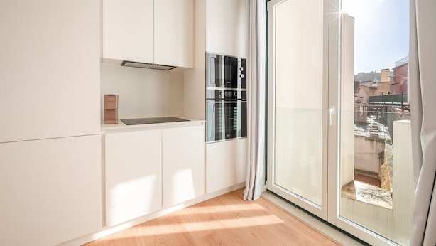 Eine moderne Küche mit weißen Schränken, einem eingebauten Ofen und einem großen Fenster mit Blick auf Gebäude.
