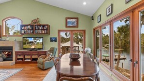 A spacious living room with a fireplace, television, and a dining area with a view of a lake. - Fisherman's Cove -Waterfront home with private dock on the River sleeps 10 (Steinhatchee)