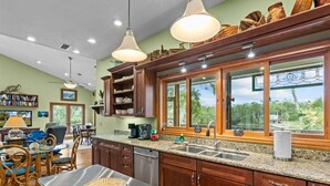 A spacious kitchen with granite countertops, wooden cabinets, and large windows offering a view of the outdoors. - Fisherman's Cove -Waterfront home with private dock on the River sleeps 10 (Steinhatchee)