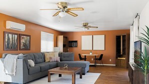A living room with a sectional sofa, a coffee table, two ceiling fans, a TV, and a dining area with a table and chairs.