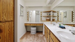 A bathroom with a wooden vanity, a large mirror with lights, and a sink.