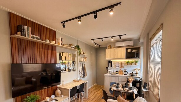 A modern living room with a flat-screen TV, wooden flooring, a sofa, a dining area, and a kitchen with wooden cabinets. - Moderno Est dio Frei Caneca a 1 km da Av Paulista (São Paulo)